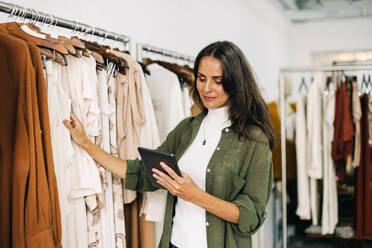 Shop owner conducting a quality control check in her clothing boutique using her digital tablet. Business woman carefully inspecting each garment to ensure that her customers receive the best items. - JLPSF30249