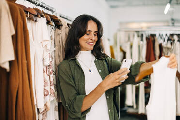 Small business owner taking a picture of a clothing item in her store in order to advertise it to her followers on social media. Female entrepreneur marketing her fashion store online. - JLPSF30253