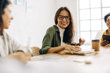 Successful business woman smiling confidently at the camera, engaged in a team meeting with her colleagues in a boardroom. Group of female entrepreneurs working as a team to grow their startup. - JLPSF30266