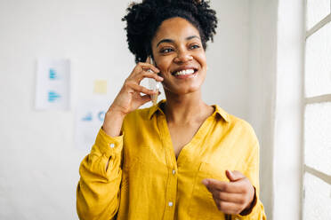 Erfolgreiche Geschäftsfrau lächelt, während sie ein Telefongespräch mit ihren Geschäftspartnern führt. Glückliche junge Frau, die in einem modernen Büro Pläne für ein Projekt macht. - JLPSF30268