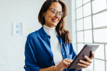 Berufstätige Frau lächelt, während sie ein digitales Tablet in einem Büro benutzt. Geschäftsfrau, die mobile Apps nutzt, um Projekte für ihr Startup zu planen, zu organisieren und abzuschließen - JLPSF30278