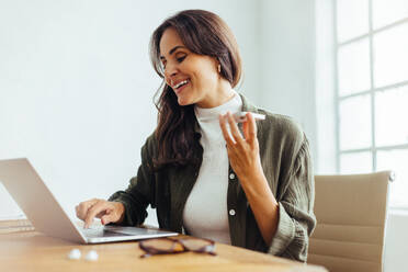 Professional business woman happily engages in conversation over the phone, using a laptop to plan and organise a collaboration with her business associates. Female entrepreneur working in her office. - JLPSF30296