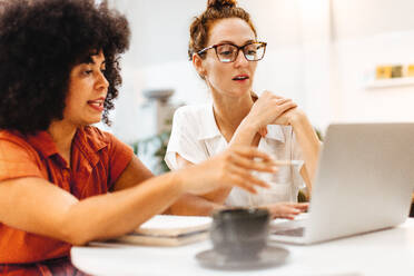 Zwei Geschäftspartnerinnen besprechen ihre Arbeit an einem Laptop in einem Café. Eine Geschäftsfrau und ihr Kunde sitzen zusammen und machen ein Brainstorming während eines informellen Treffens. - JLPSF30300