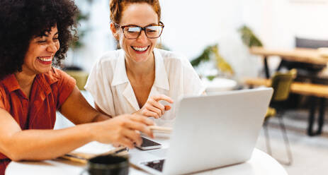 Zwei glückliche Frauen beim Brainstorming und bei der gemeinsamen Arbeit an einem Laptop in einem Coworking Space. Erfolgreiche Geschäftsleute teilen ihr Fachwissen und arbeiten gemeinsam an einem Projekt. - JLPSF30301