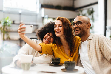 Friends take a fun selfie together in a coffee shop, laughing and enjoying each other's company as they capture a lighthearted moment. Group of diverse young people enjoying a happy social gathering. - JLPSF30313
