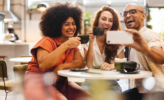 Eine Gruppe von Freunden genießt Kaffee, Lachen und Selfies, während sie in der positiven und entspannten Atmosphäre ihres Lieblingscafés Erinnerungen schaffen - JLPSF30315