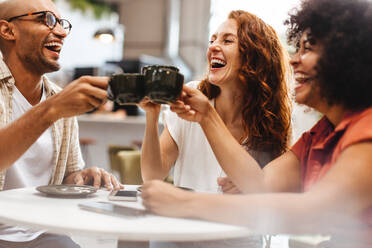 Eine Gruppe glücklicher Freunde stößt mit einer warmen Tasse Kaffee auf ihre Freundschaft an und genießt die gemeinsame Zeit. Freunde lachen und genießen die Gesellschaft des anderen. - JLPSF30316