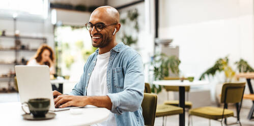 Erfolgreicher Geschäftsmann, der von einem Café aus arbeitet und seinen Laptop benutzt, um seine Aufgaben online zu erledigen. Ein glücklicher Geschäftsmann, der es genießt, in einer entspannten, mit dem Internet verbundenen Umgebung zu sein. - JLPSF30318