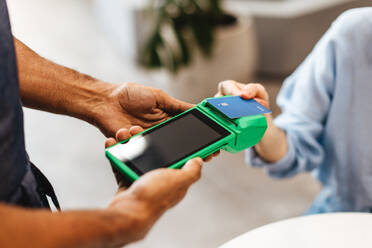 Frau, die in einem Café ihre Kreditkarte über ein Kartenlesegerät scannt, um eine Zahlung an den Kellner zu leisten. Eine Kundin, die ihre Rechnung mit einer elektronischen Transaktion begleicht. - JLPSF30336