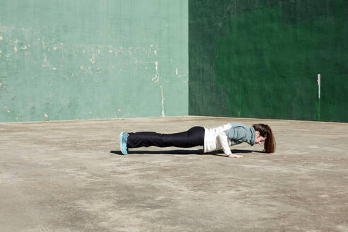 Seitenansicht einer flexiblen Frau in Sportkleidung, die sich mit geschlossenen Augen dehnt und Yoga auf der Straße praktiziert - ADSF43936