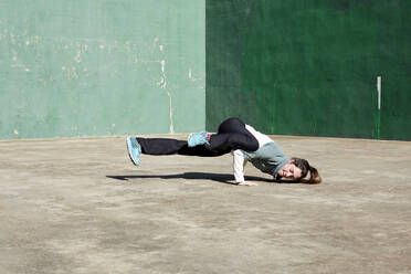 Fokussierte junge Frau in Sportkleidung, die eine fliegende Taube posiert, während sie Yoga an einer verwitterten Wand übt - ADSF43937