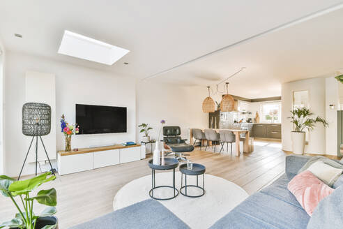 Inneneinrichtung eines modernen, geräumigen Wohnzimmers mit bequemem Sofa, runden Couchtischen und TV in der Nähe der Küchenzeile - ADSF43975
