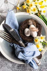 From above easter dinner table set with eggs in the nest and daffodil flowers on concrete background - ADSF43983