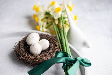 Von oben Ostern Abendessen Tisch mit Eiern im Nest und Narzissen Blumen auf konkreten Hintergrund gesetzt - ADSF43984