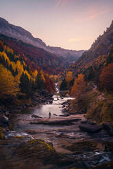 Unrecognizable tourist standing on rock in spectacular scenery of calm river surrounded by colorful autumn trees in highlands in evening time in Pyrenees - ADSF44017