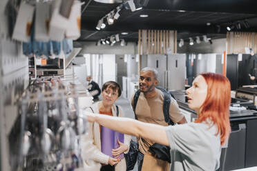 Saleswoman advising customers in buying modern appliance at electronics store - MASF36649