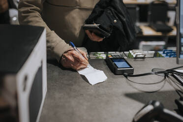 Mittelteil eines älteren Mannes, der eine Rechnung mit einem Kreditkartenleser an der Kasse eines Elektronikgeschäfts unterschreibt - MASF36681