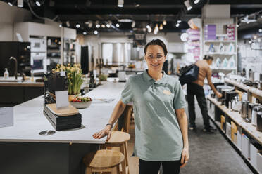 Portrait of confident saleswoman standing by table in appliances store - MASF36685