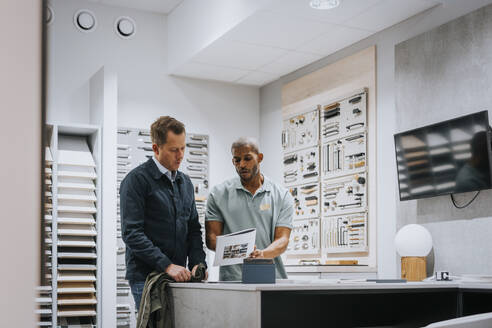 Salesman discussing with mature man over brochure at store - MASF36690