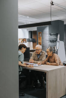 Ein älteres Ehepaar diskutiert mit einer Innenarchitektin an einem Schreibtisch im Geschäft - MASF36695