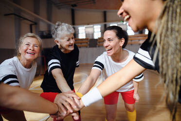 A group of multigenerational women in gym stacking hands together, sport team players. - HPIF09346