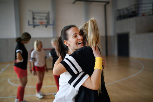 Eine Gruppe junger und älterer Frauen, Sportspielerinnen, in der Turnhalle, die den Sieg feiern und sich umarmen. - HPIF09350