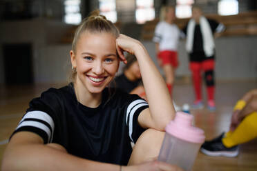 Porträt einer jungen hübschen Frau, die sich nach einem Spiel mit ihren Mannschaftskameraden in der Sporthalle ausruht. - HPIF09362