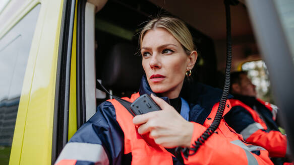 Portrait of a young woman doctor sitting and talking in to walkie-talkie in ambulance car. - HPIF09405