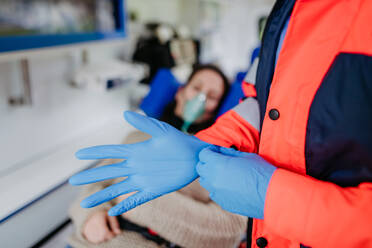 Nahaufnahme eines Rettungssanitäters, der vor der Untersuchung eines Patienten chirurgische Handschuhe anzieht. - HPIF09439