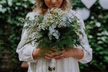 Eine Nahaufnahme vonHochzeit Bouquet in den Händen der Braut beim Empfang draußen im Hinterhof - HPIF09477