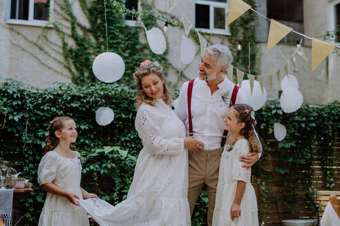 Kleine Tochter hält ein Hochzeitskleid Zug ihre Mutter im Hinterhof Partei. - HPIF09500