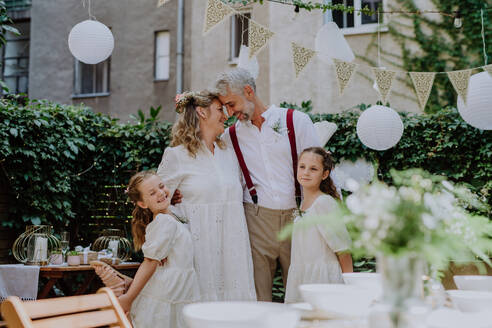 Reife Braut und Bräutigam posieren mit ihren Töchtern bei der Hochzeitsfeier draußen im Hinterhof. - HPIF09503