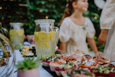 Eine Nahaufnahme des Dessertbuffets bei einer kleinen Hochzeitsfeier im Hinterhof, kleine Mädchen im Hintergrund. - HPIF09519