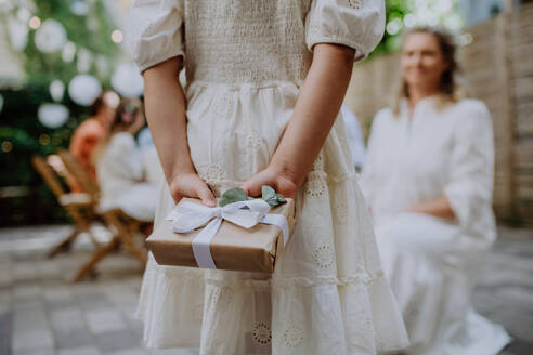 Rückansicht eines kleinen Kindes, das der reifen Braut auf einer Hochzeitsparty im Hinterhof ein Hochzeitsgeschenk überreicht. - HPIF09537