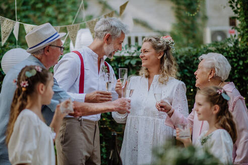 Eine reife Braut und ein reifer Bräutigam stoßen mit den Gästen auf der Hochzeitsfeier im Hinterhof an. - HPIF09557