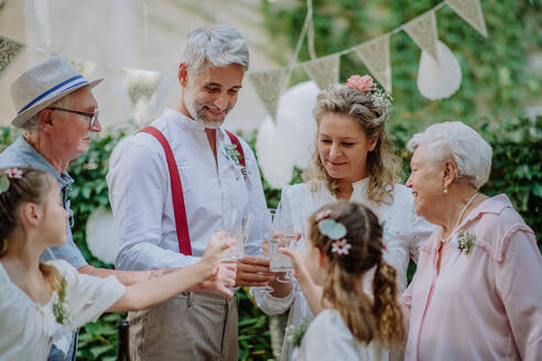 Eine reife Braut und ein reifer Bräutigam stoßen mit den Gästen auf der Hochzeitsfeier im Hinterhof an. - HPIF09559