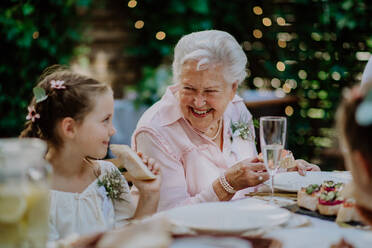 Hochzeitsgäste, die an einem Tisch sitzen und bei einem Empfang im Garten essen und trinken. - HPIF09560