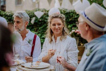 Eine reife Braut und ein reifer Bräutigam stoßen mit den Gästen auf der Hochzeitsfeier im Hinterhof an. - HPIF09564