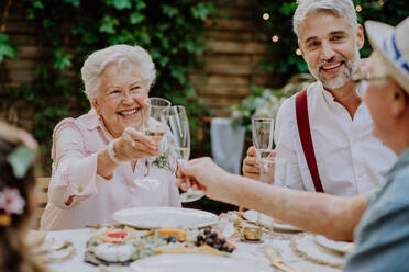 Mature groom toasting with his parents in law at wedding reception outside in backyard. - HPIF09565