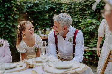 Glücklicher Bräutigam im Gespräch und lächelnd mit seiner kleinen Tochter während Garten Hochzeitsparty. - HPIF09573