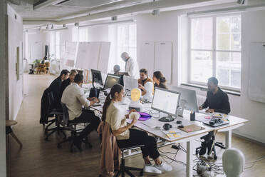 Professors discussing with PhD students over computer at desk in innovation lab - MASF36722