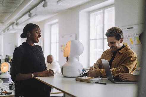 Multirassische lächelnde Studenten mit beleuchtetem sozialen Roboter am Schreibtisch im Innovationslabor - MASF36742