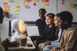 Lächelnde, gemischtrassige Studenten betrachten einen beleuchteten modernen Roboter im Innovationslabor - MASF36747
