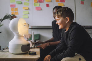 Lächelnder Junge kommuniziert mit beleuchtetem KI-Roboter im Innovationslabor - MASF36750