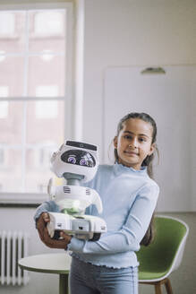 Porträt eines Mädchens, das einen sozialen Roboter trägt, der im Innovationslabor steht - MASF36753
