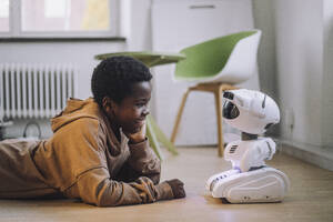 Lächelnder Junge im Gespräch mit einem KI-Roboter, während er in einem Innovationslabor auf dem Boden liegt - MASF36755