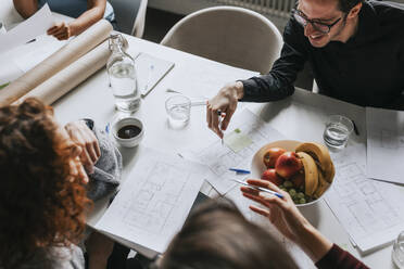 Hohe Winkel Ansicht der Geschäftsleute Planung Strategie am Schreibtisch mit Früchten im Büro - MASF36772