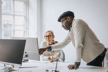 Side view of businessman explaining female colleague over computer at desk in office - MASF36809