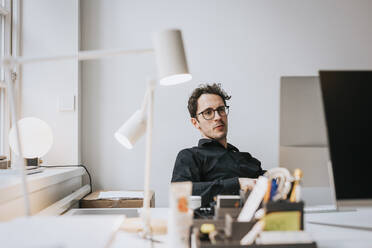 Geschäftsmann mit Brille sitzt am Schreibtisch im Büro - MASF36813