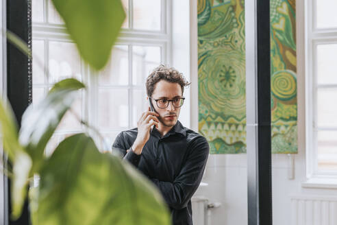 Nachdenklicher Geschäftsmann, der im Büro mit seinem Smartphone telefoniert - MASF36823